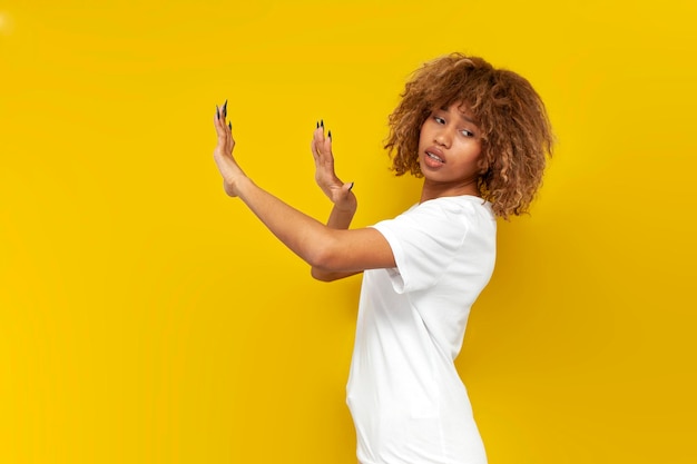 Young curly american girl refuse and avoid with hands on yellow isolated background