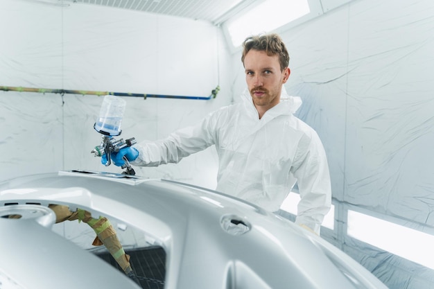 Young curly car painter varnishes car bumper Man works in a spray booth