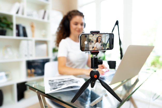 Young curly female blogger recording video at table at home