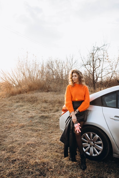 사진 가을의 자연을 배경으로 오렌지색 스웨터를 입은 어린 곱슬한 소녀