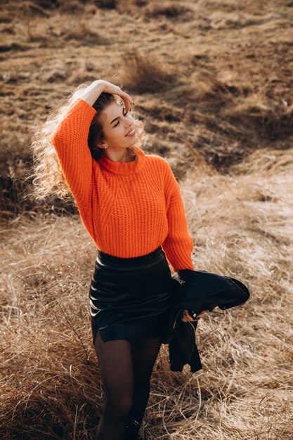 Young curly girl in an orange sweater against the backdrop of autumn nature