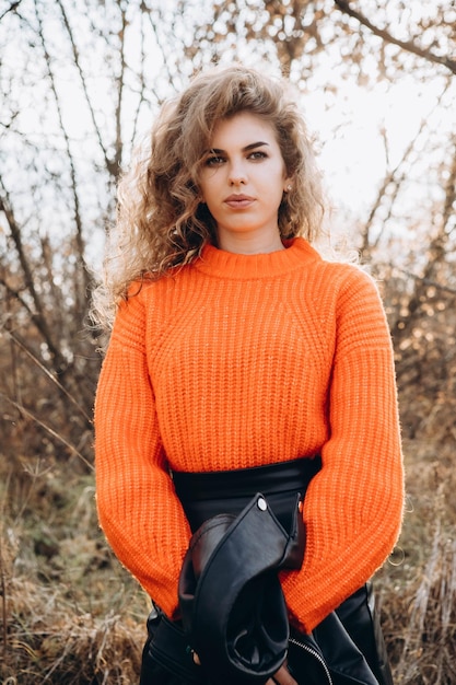 Foto giovane ragazza riccia con un maglione arancione sullo sfondo della natura autunnale