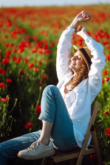 Young curly girl posing in a poppy field sitting on a chair Summertime