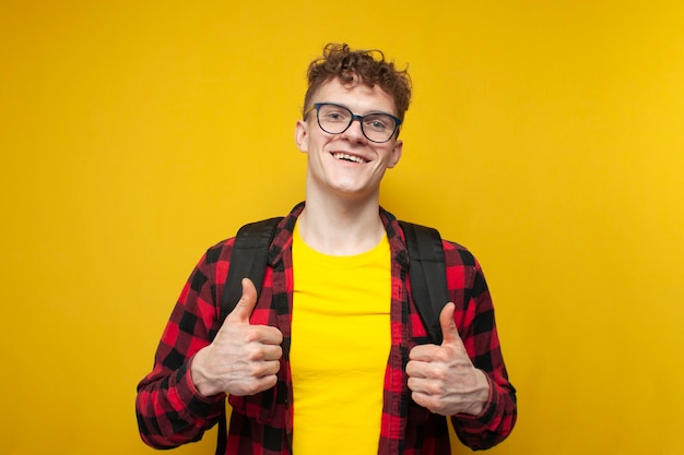 young curly guy student in glasses with a backpack stands on a yellow background