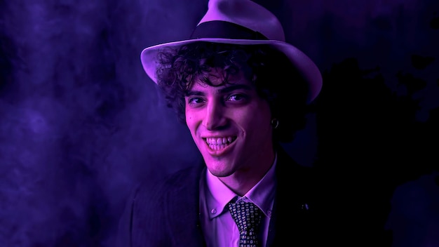 Young curly haired brunette man with hat and suit looks at the camera and smiles