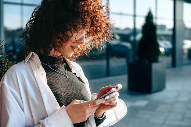 Young curly haired freelancer is chatting with somebody about a new project while posing outside