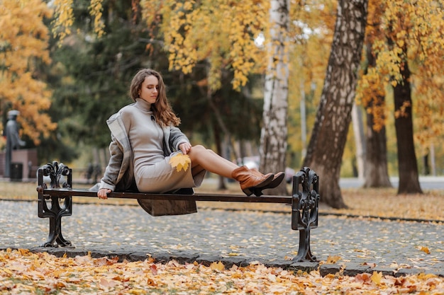 Young curly haired girl in a gray dress sits on a bench in an autumn park