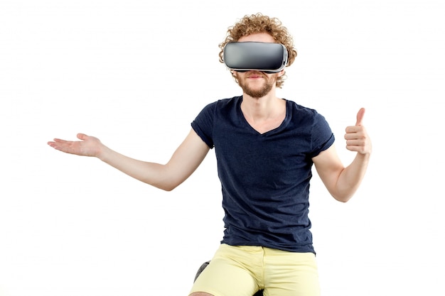 Young curly-haired man using a VR headset and experiencing virtu