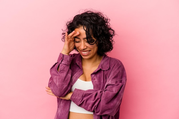 Young curly latin woman isolated on pink background blink at the camera through fingers, embarrassed covering face.