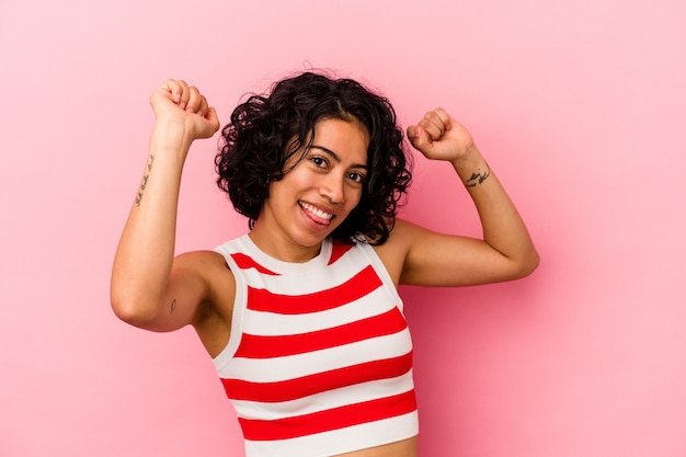 Young curly latin woman isolated on pink background celebrating a special day, jumps and raise arms with energy.