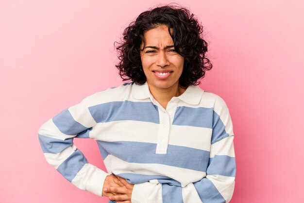 肝臓の痛み、胃の痛みを持つピンクの背景に分離された若い巻き毛のラテン女性。