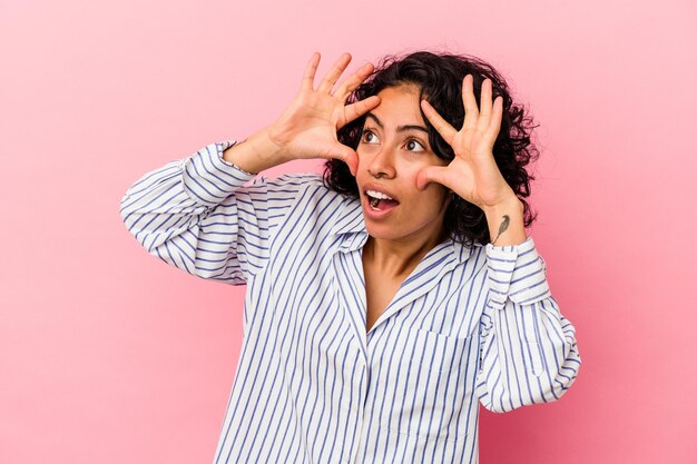 Young curly latin woman isolated on pink background keeping eyes opened to find a success opportunity.