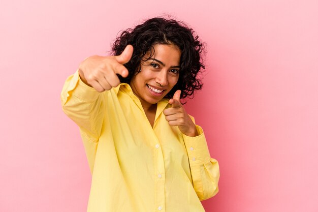 Young curly latin woman isolated on pink background pointing to front with fingers.