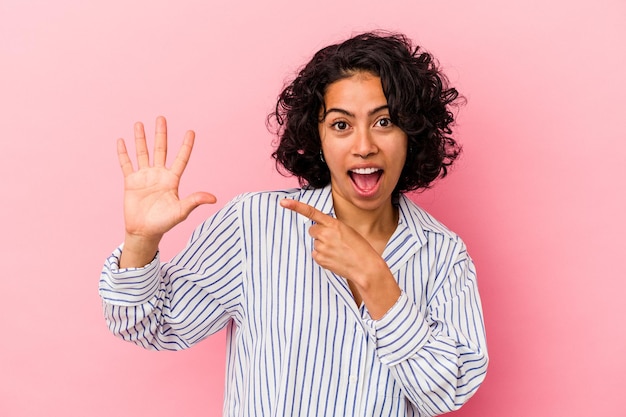 Young curly latin woman isolated on pink background smiling cheerful showing number five with fingers.