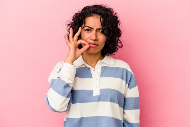 Young curly latin woman isolated on pink background with fingers on lips keeping a secret.