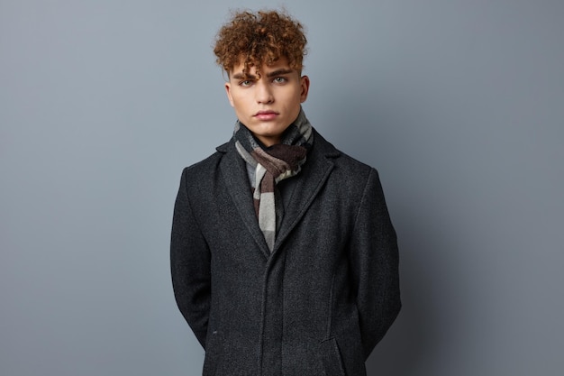 Young curly man in a coat in the studio posing on a gray background