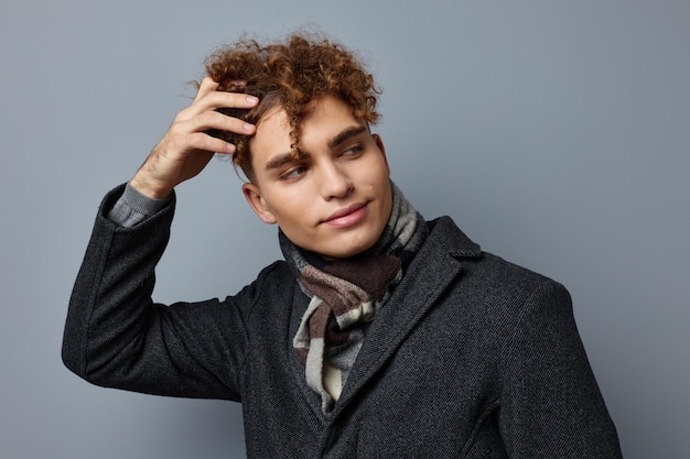 Young curly man in a coat in the studio posing on a gray background