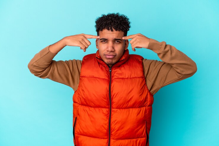 Photo young curly man isolated on blue focused on a task, keeping forefingers pointing head