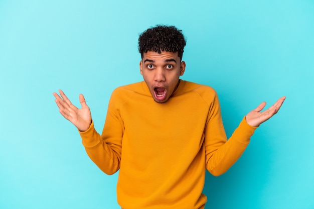 Young curly man isolated on blue surprised and shocked