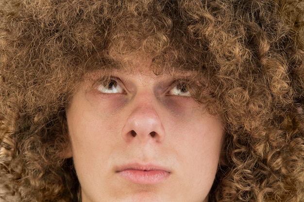 Young curly man looks at his hair with his eyes up. very lush male guy hair