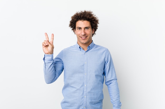 Photo young curly mature man wearing an elegant shirt joyful and carefree showing a peace symbol with fingers.