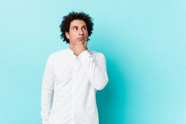 young curly mature man wearing an elegant shirt looking sideways with doubtful and skeptical expression.