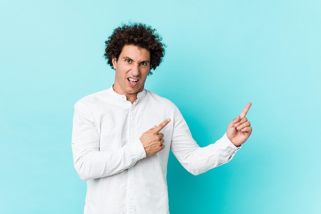 Young curly mature man wearing an elegant shirt pointing with forefingers to a copy space, expressing excitement and desire.