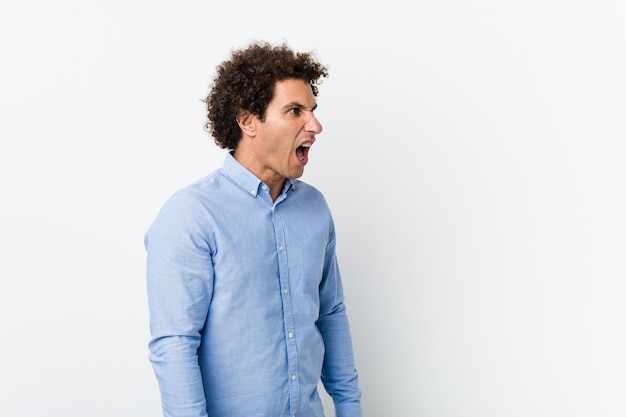 Young curly mature man wearing an elegant shirt shouting towards a copy space