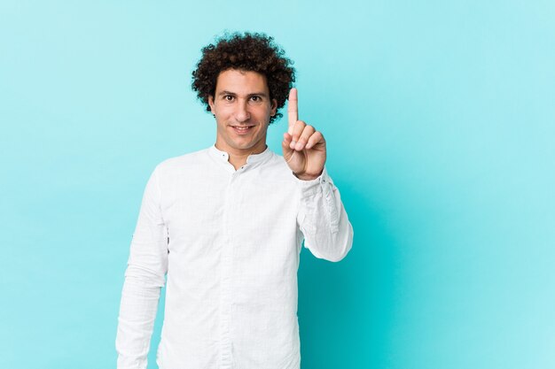 Young curly mature man wearing an elegant shirt showing number one with finger.