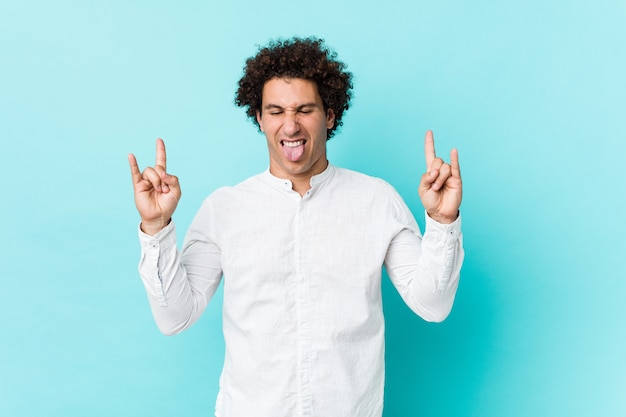 Young curly mature man wearing an elegant shirt showing rock gesture with fingers