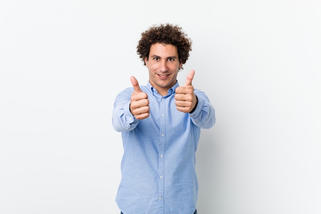 Young curly mature man wearing an elegant shirt with thumbs ups, cheers about something, support and respect concept.