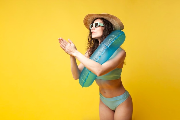 Young curly slender brunette girl in a blue swimsuit in summer with an inflatable swimming ring