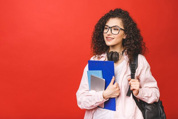 書籍やタブレットを保持しているバックパックを着ている若い巻き毛学生女性