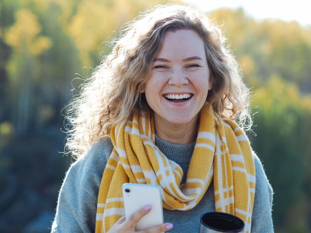 Photo young curly woman freelancer smiling with phone on her hands at mountain in autumn