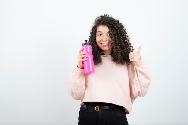 Young curly woman in sweater holding pink water bottle.