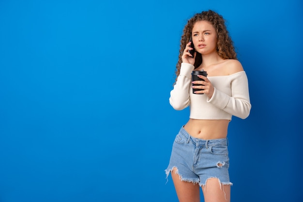 Young curly woman talking on the phone against blue background