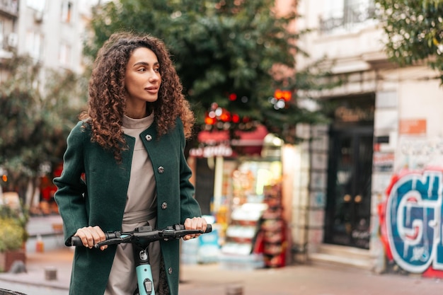 Фото Молодая кудрявая женщина с электрическим скутером в городе
