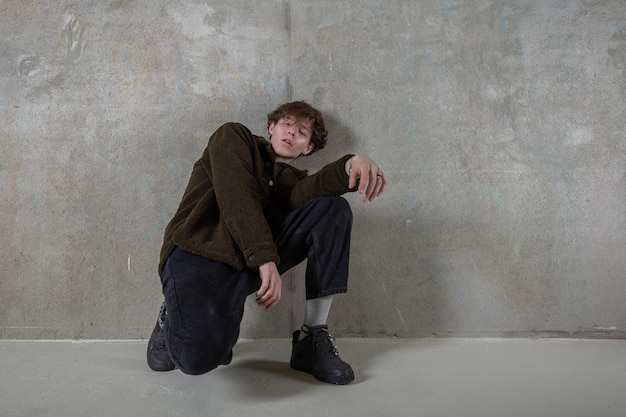 Young curlyhaired caucasian guy sitting at the concrete wall in relaxing pose