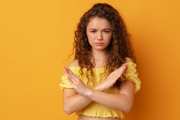 Young curlyhaired woman standing with crossed hands against yellow background