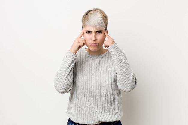 Young curvy caucasian woman focused on a task, keeping forefingers pointing head.