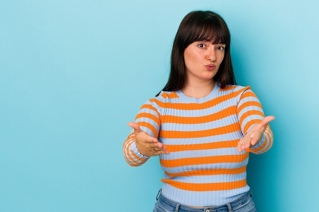 Young curvy caucasian woman isolated on blue background folding lips and holding palms to send air kiss.