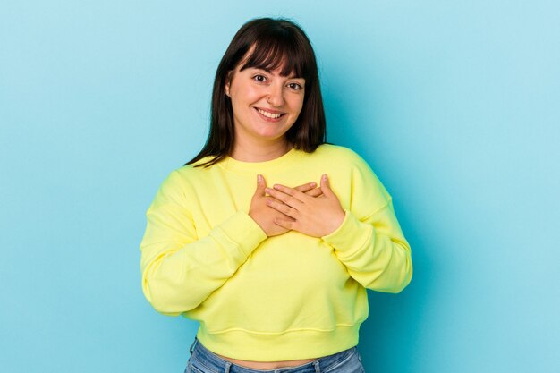 Young curvy caucasian woman isolated on blue background laughing keeping hands on heart, concept of happiness.