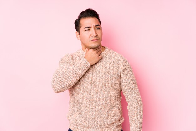 Young curvy man posing in a pink wall isolated suffers pain in throat due a virus or infection.