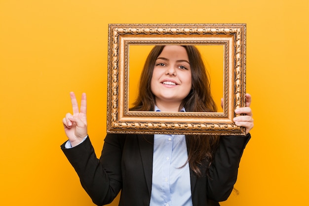 Young curvy plus size business woman holding a frame showing number two with fingers
