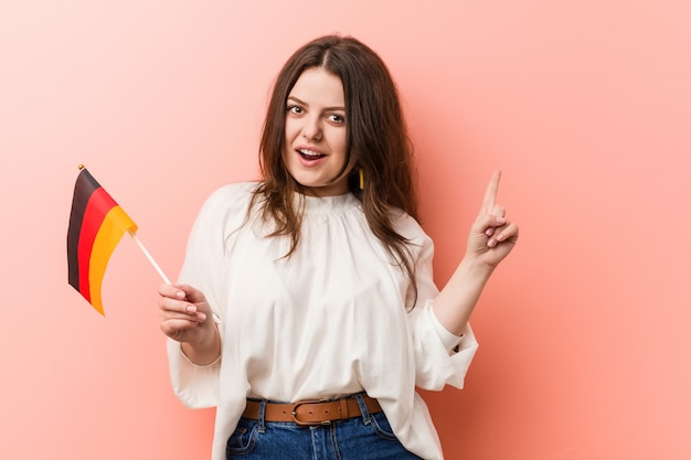 Young curvy plus size woman holding a germany flag smiling cheerfully pointing with forefinger away.