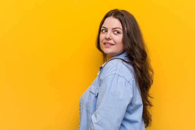 Young curvy plus size woman looks aside smiling, cheerful and pleasant.