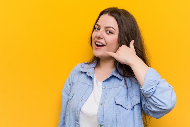 Young curvy plus size woman showing a mobile phone call gesture with fingers.