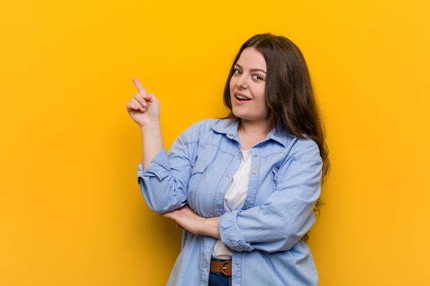 Young curvy plus size woman smiling cheerfully pointing with forefinger away.