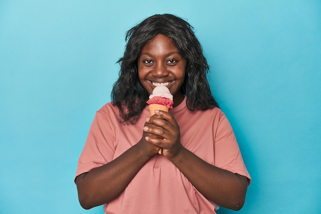 Young curvy woman enjoying icecream on a blue backdrop
