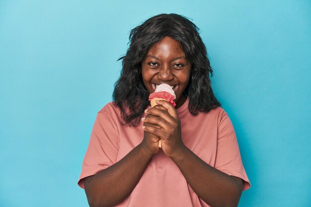 Young curvy woman enjoying icecream on a blue backdrop